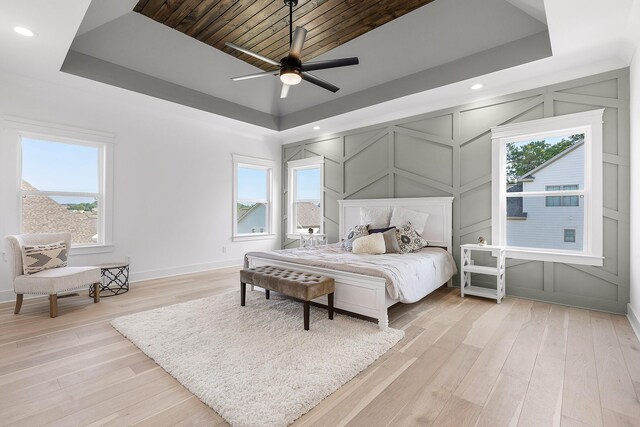 bedroom featuring light wood-style floors, a tray ceiling, and a decorative wall