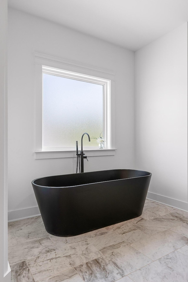 bathroom featuring a wealth of natural light, a freestanding bath, and baseboards