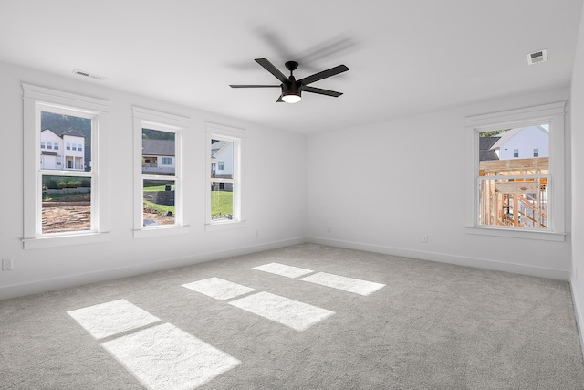 carpeted spare room featuring ceiling fan, visible vents, and baseboards