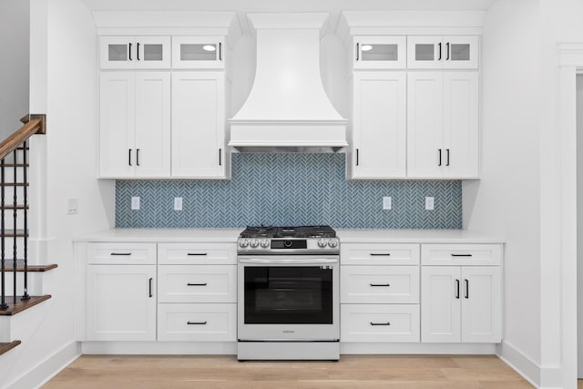 kitchen featuring light countertops, glass insert cabinets, white cabinets, premium range hood, and stainless steel gas range oven