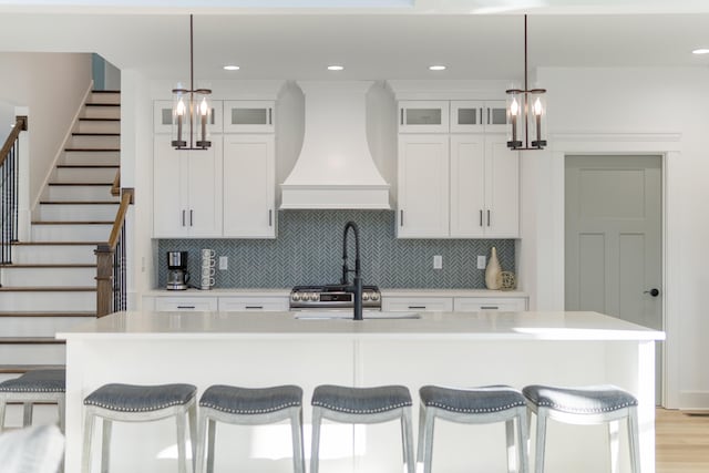 kitchen featuring tasteful backsplash, a kitchen island with sink, custom exhaust hood, and light countertops