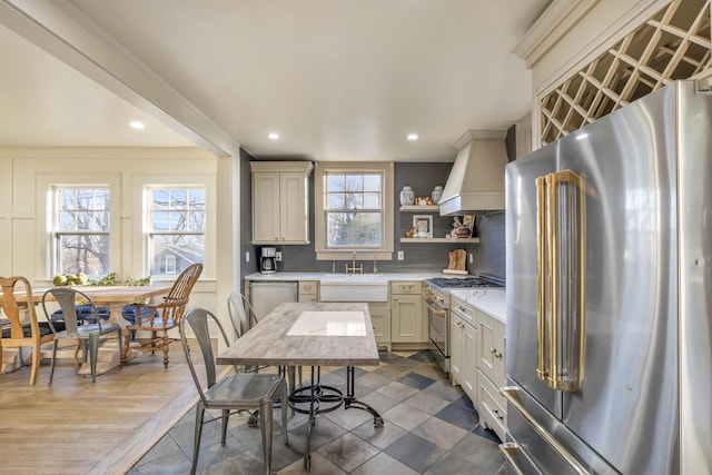 kitchen with light countertops, appliances with stainless steel finishes, backsplash, open shelves, and custom range hood