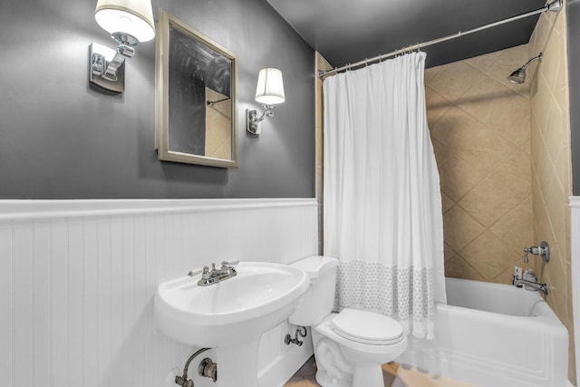 bathroom with shower / bath combo, wainscoting, a sink, and toilet