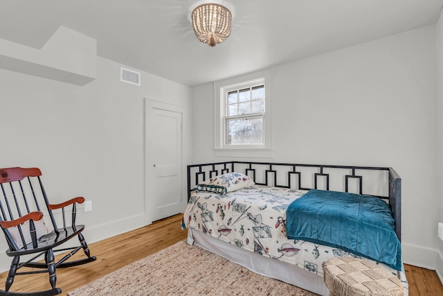 bedroom with baseboards, visible vents, and wood finished floors