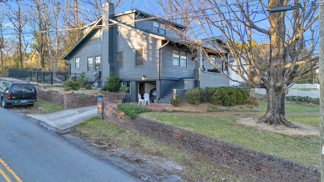 view of side of home featuring fence, stairs, driveway, a lawn, and a chimney