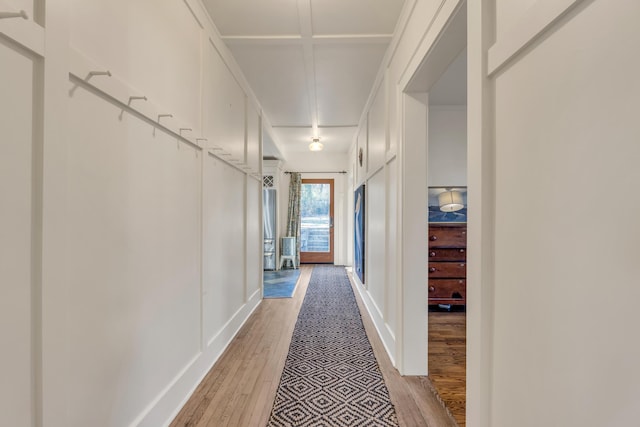 corridor featuring ornamental molding, light wood-style flooring, and a decorative wall