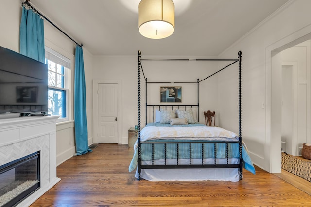 bedroom with ornamental molding, baseboards, a tiled fireplace, and wood finished floors