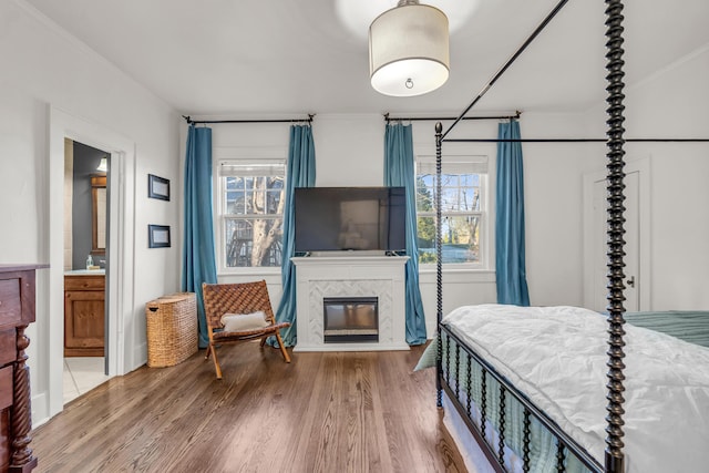 bedroom with ensuite bath, multiple windows, a tiled fireplace, and wood finished floors