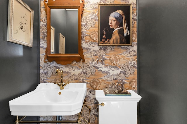 half bath featuring toilet, wallpapered walls, and a sink