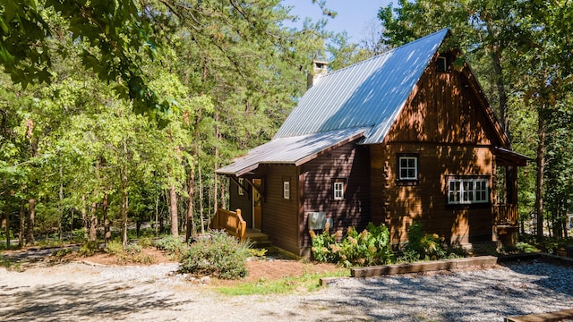 view of property exterior featuring a chimney, metal roof, and a wooded view