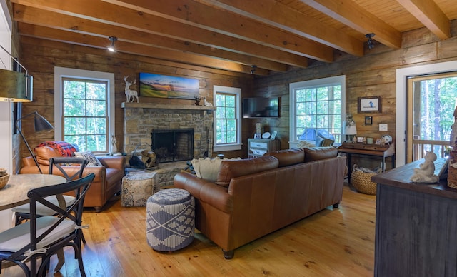 living room featuring light wood-style flooring, beam ceiling, a stone fireplace, and wooden walls