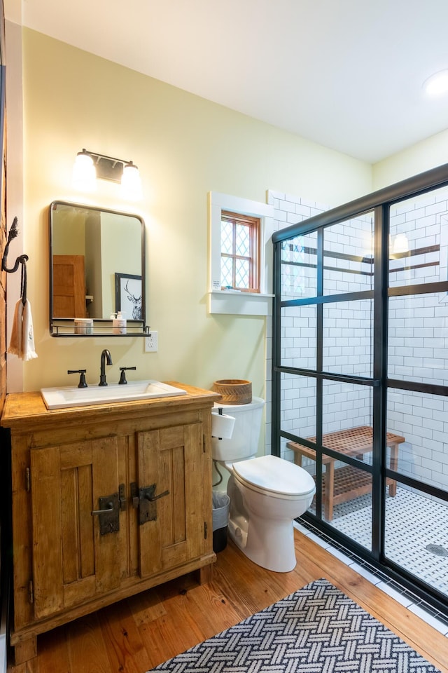 bathroom featuring toilet, a tile shower, wood finished floors, and vanity