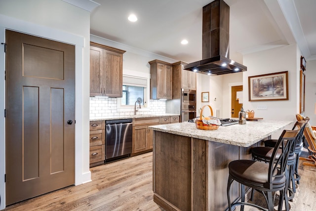 kitchen featuring decorative backsplash, appliances with stainless steel finishes, a breakfast bar area, island exhaust hood, and light wood-style floors