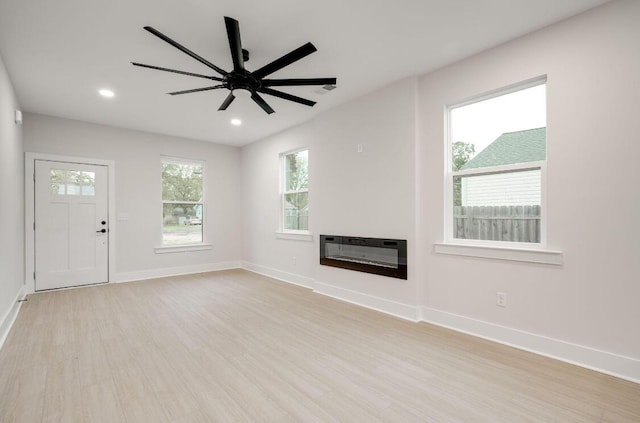 unfurnished living room with baseboards, a glass covered fireplace, ceiling fan, light wood-type flooring, and recessed lighting