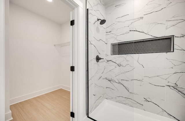 bathroom featuring wood finished floors, a marble finish shower, a walk in closet, and baseboards