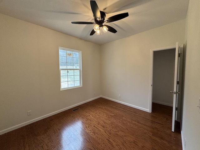 unfurnished room with dark wood-style floors, a ceiling fan, visible vents, and baseboards