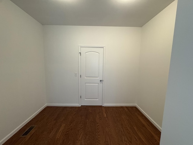 spare room featuring dark wood-type flooring, visible vents, and baseboards