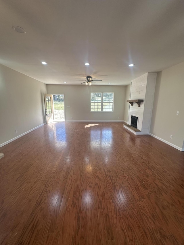 unfurnished living room featuring dark wood-type flooring, a fireplace, a ceiling fan, and baseboards