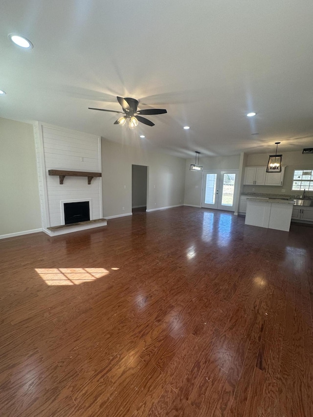 unfurnished living room featuring a fireplace, dark wood finished floors, a wealth of natural light, and a ceiling fan