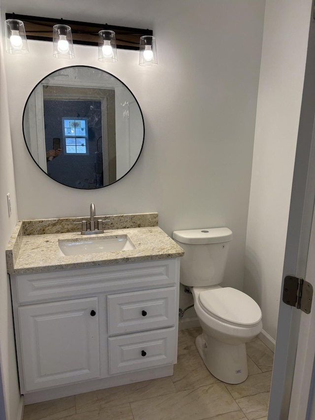 half bathroom with baseboards, vanity, and toilet