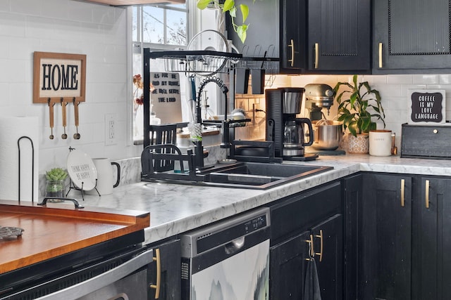 kitchen featuring backsplash, light countertops, dark cabinetry, stainless steel dishwasher, and a sink