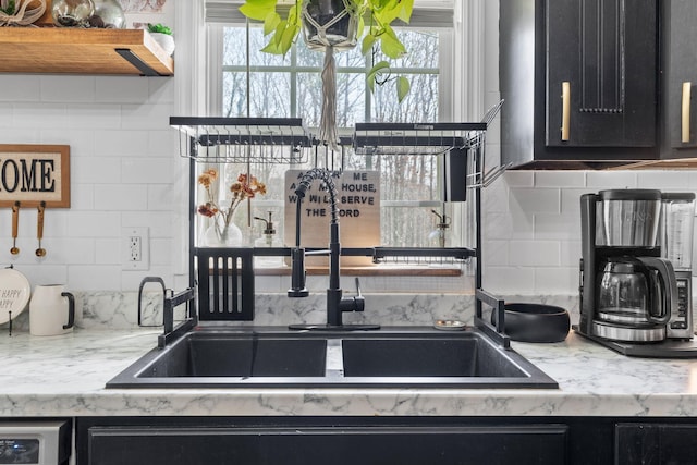 kitchen with dark cabinets, a sink, backsplash, and light stone counters