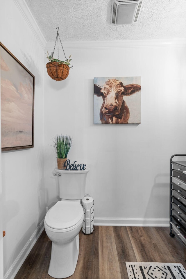 bathroom featuring visible vents, toilet, wood finished floors, crown molding, and a textured ceiling