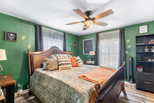 bedroom with a textured ceiling, ceiling fan, multiple windows, and wood finished floors