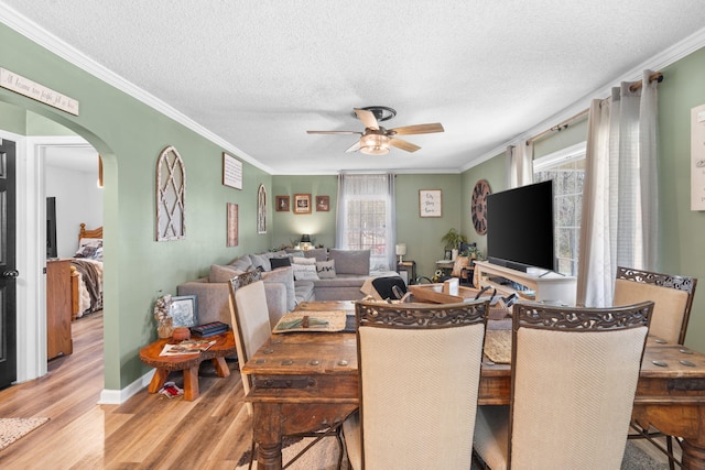 dining space with arched walkways, a ceiling fan, ornamental molding, wood finished floors, and a textured ceiling