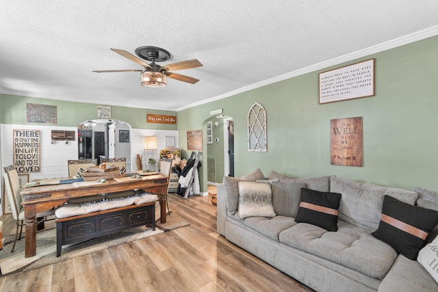 living area with crown molding, arched walkways, ceiling fan, and wood finished floors