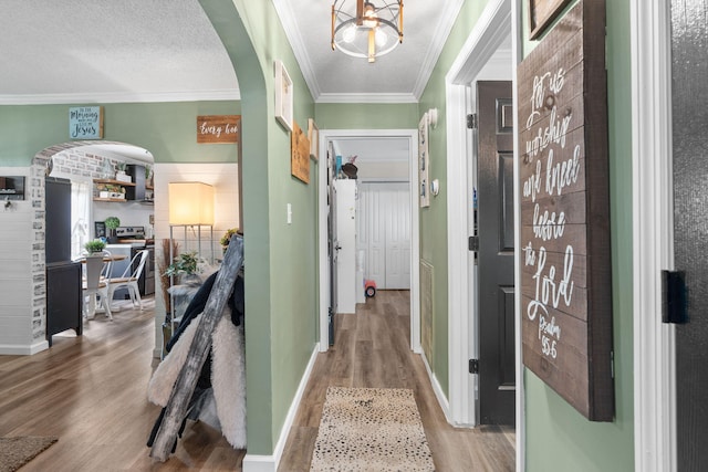 corridor featuring arched walkways, ornamental molding, a textured ceiling, and wood finished floors