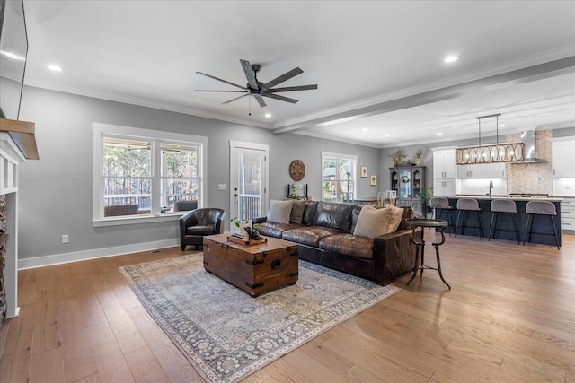 living area featuring baseboards, light wood-style floors, ceiling fan, and ornamental molding