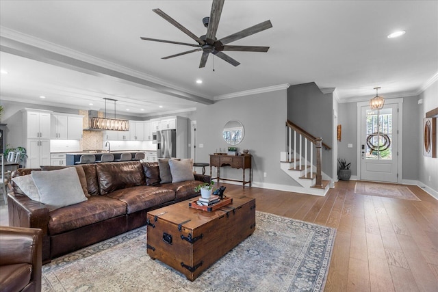 living room with stairway, a ceiling fan, baseboards, light wood-style flooring, and ornamental molding