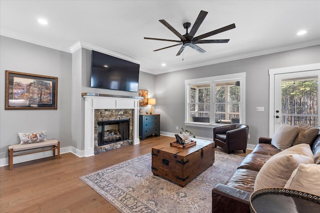 living room featuring crown molding, baseboards, a fireplace, wood finished floors, and a ceiling fan