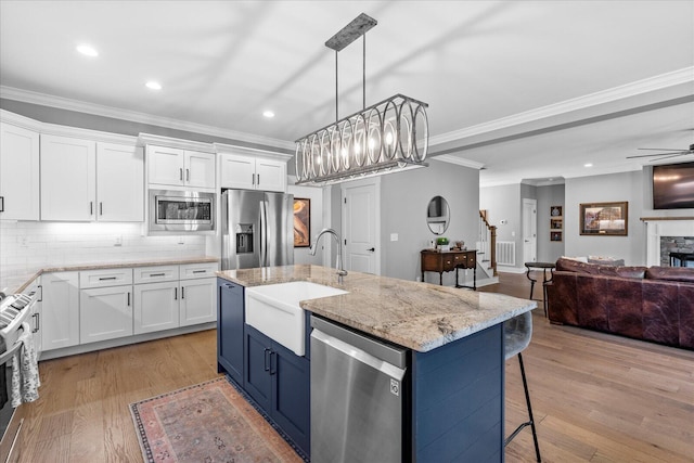 kitchen with light wood finished floors, a sink, white cabinets, appliances with stainless steel finishes, and open floor plan