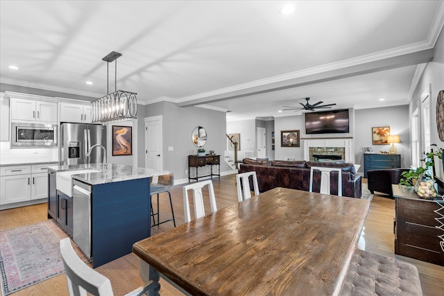 dining area with light wood-style floors, a stone fireplace, a ceiling fan, and crown molding