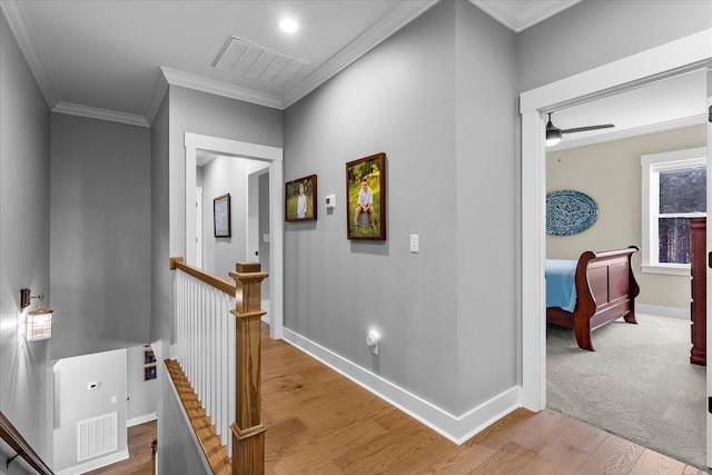 hall with visible vents, an upstairs landing, ornamental molding, and light wood-style flooring
