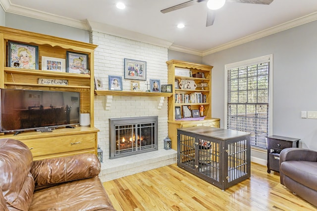 living area featuring a ceiling fan, a brick fireplace, crown molding, and wood finished floors