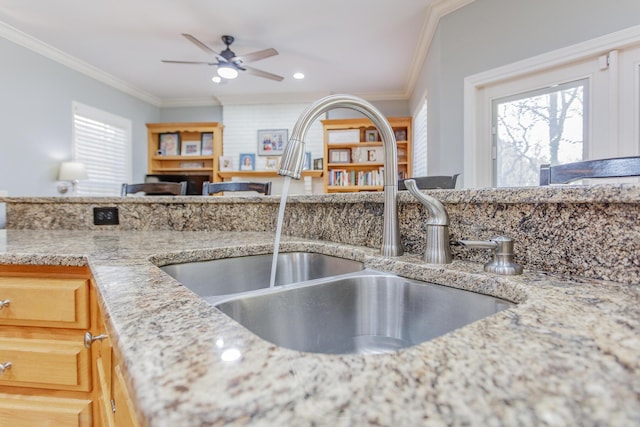 kitchen with a healthy amount of sunlight, crown molding, light stone counters, and a sink