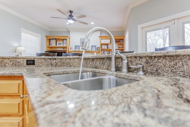 kitchen featuring ornamental molding, a sink, light stone counters, and a ceiling fan