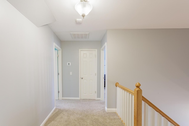 hall with carpet floors, visible vents, baseboards, and an upstairs landing