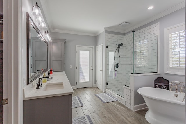 full bath with ornamental molding, wood finished floors, a freestanding bath, a shower stall, and a sink