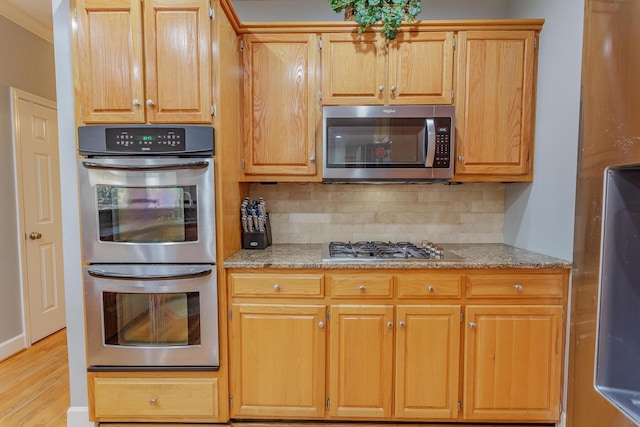 kitchen with light stone countertops, tasteful backsplash, stainless steel appliances, and light wood-style flooring