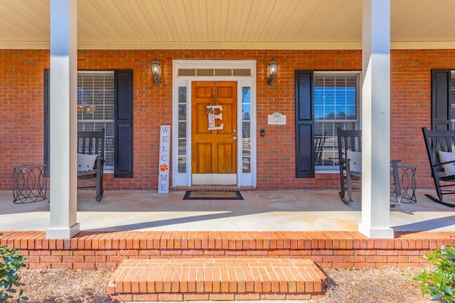 view of exterior entry featuring covered porch and brick siding