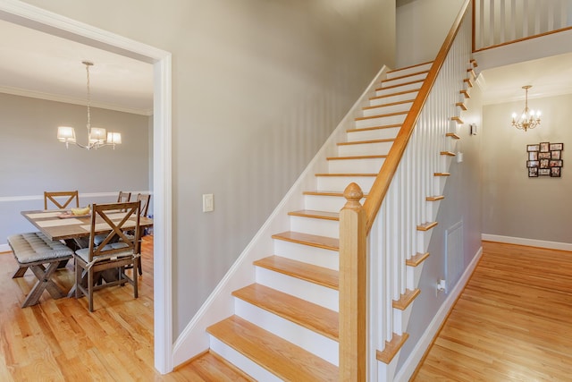 staircase featuring a chandelier, wood finished floors, visible vents, baseboards, and crown molding