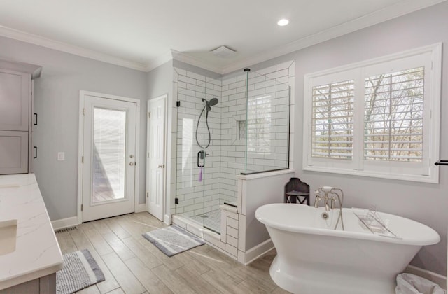 bathroom with a stall shower, baseboards, a soaking tub, ornamental molding, and wood finished floors