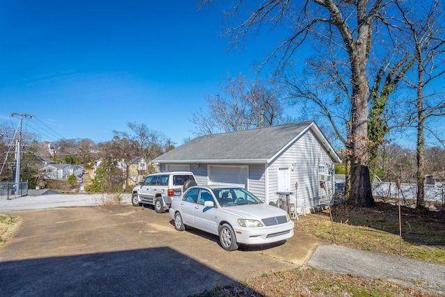 view of side of property featuring a garage, concrete driveway, and roof with shingles