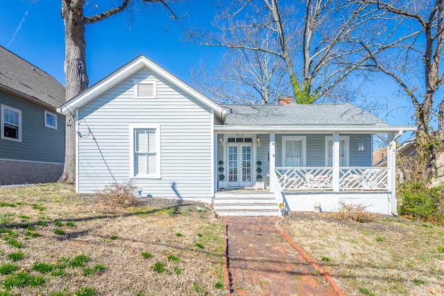 view of front of house with covered porch, roof with shingles, a chimney, and french doors