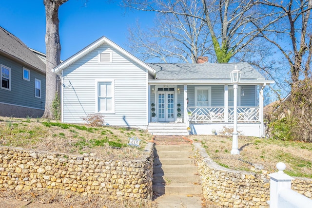 view of front of home with roof with shingles, a chimney, a porch, and french doors