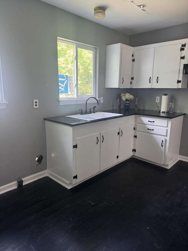 kitchen with dark countertops, a sink, dark wood-style flooring, baseboards, and white cabinetry